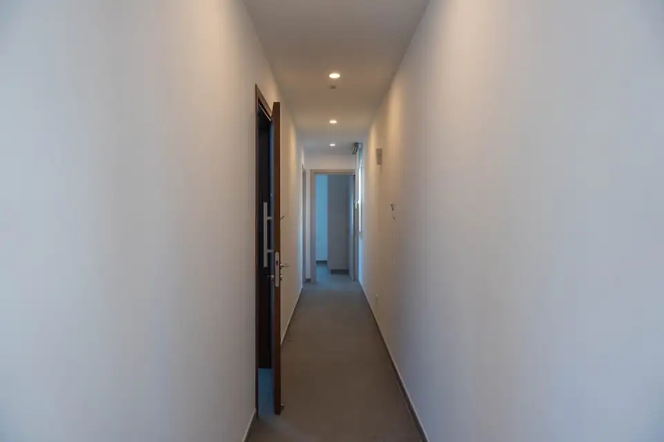 Photograph of a narrow finished internal corridor with plain white walls and a dark timber door