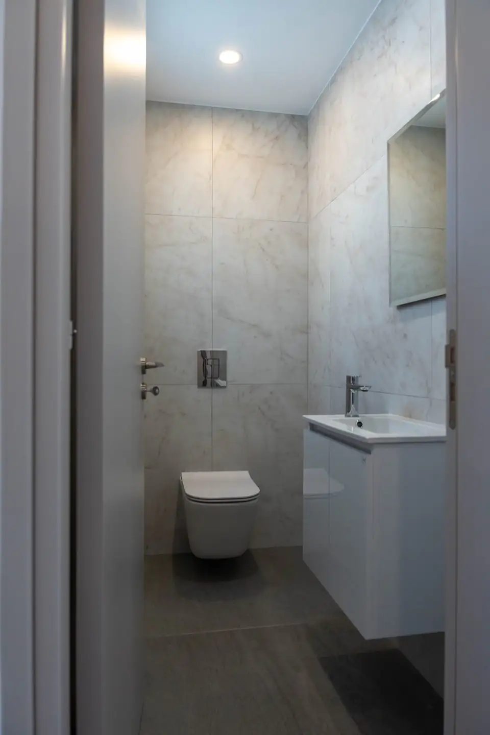 Compact guest cloakroom with marble-effect tiling, wall-hung WC and white vanity basin