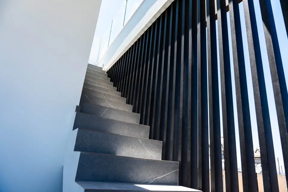 Looking up an external cantilevered stone staircase against black vertical metal railings